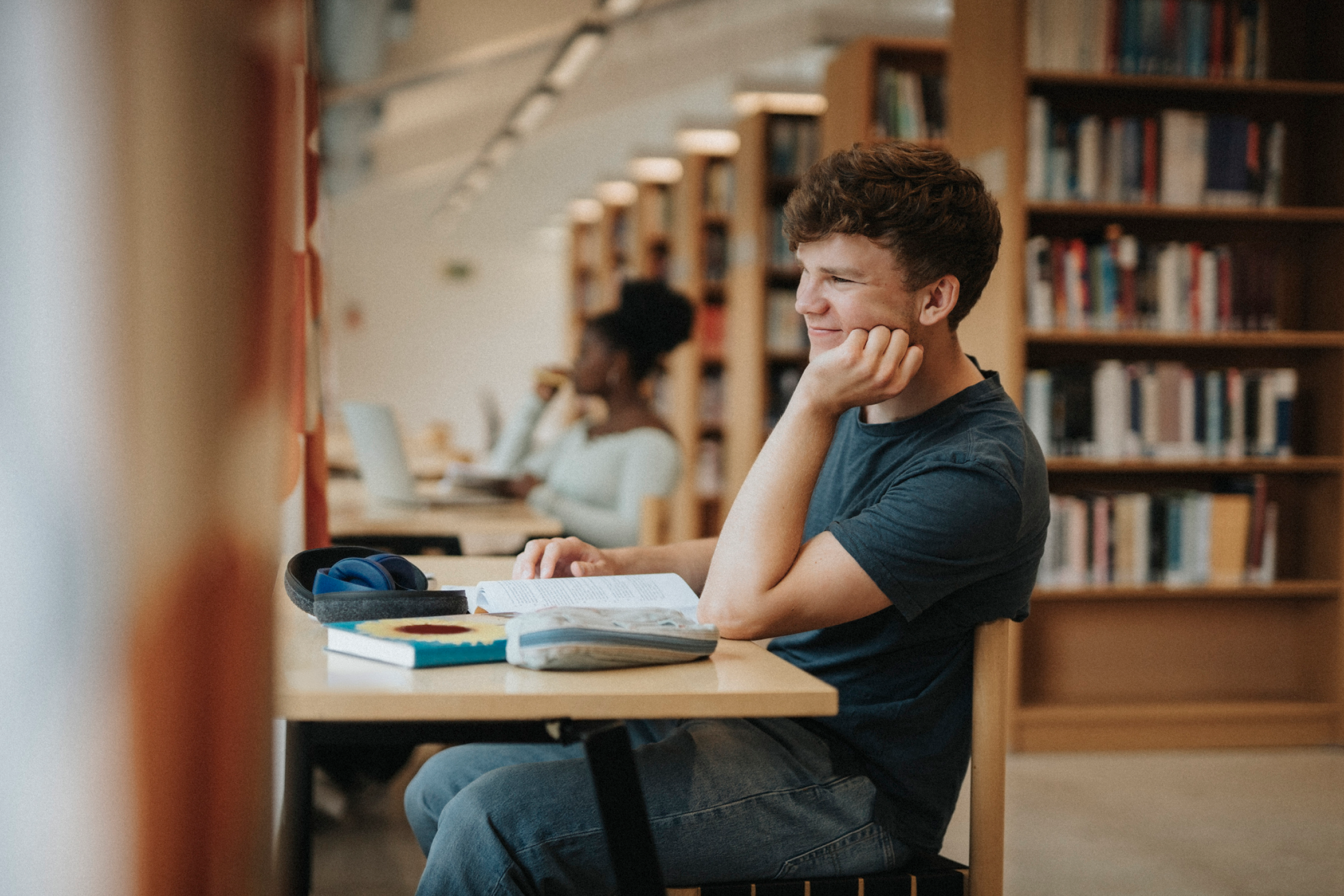 A student studying at a desk with books and a laptop in a library.